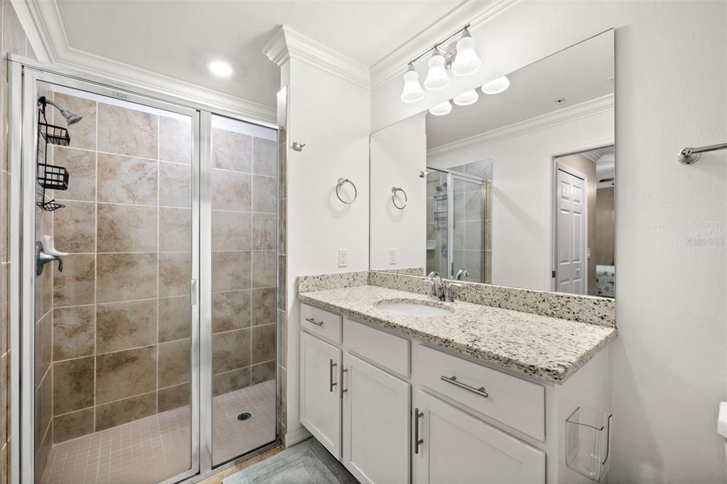 A bathroom features a tiled walk-in shower, a white vanity with granite countertops, and mirror — 43020 GREENWAY BOULEVARD UNIT 312, PUNTA GORDA, FL
