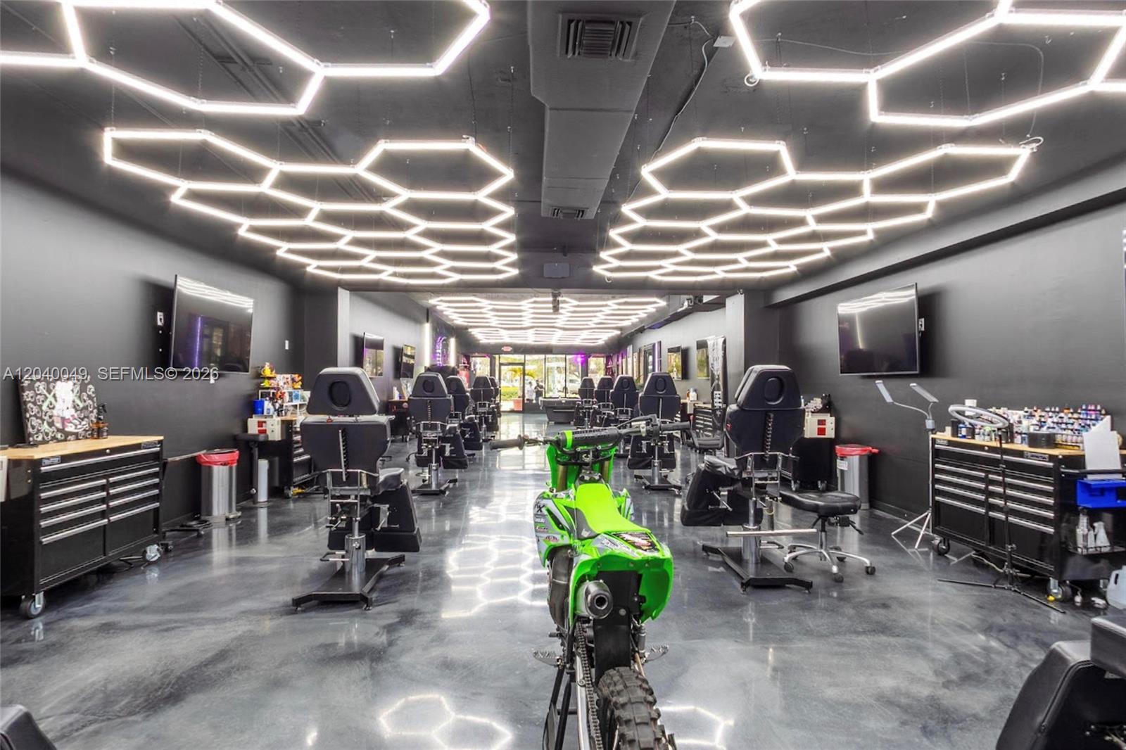 A modern tattoo studio features black walls, hexagonal ceiling lights, and a central dirt bike — 1816 Harrison St, Hollywood FL 33020, HOLLYWOOD, FL
