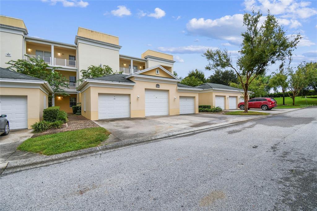 A multi-story apartment building with several ground-level garages and a red car parked nearby — 1501 NORTHERN HARRIER WAY UNIT 302, REUNION, FL