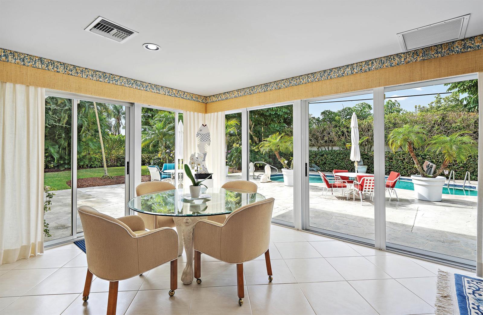 A dining area with a glass table and chairs overlooks a patio and swimming pool — 11337 Lost Tree Way, North Palm Beach FL 33408, NORTH PALM BEACH, FL