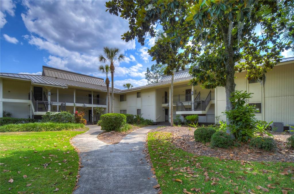 A concrete walkway leads to the entrance of a two-story apartment building with metal roofs — 29300 BAY HOLLOW DRIVE UNIT 3258, WESLEY CHAPEL, FL