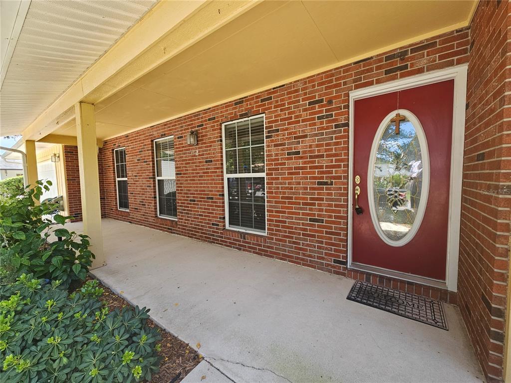 A red front door with an oval glass insert sits on a brick porch — 1311 GLENVIEW LANE, LAKELAND, FL