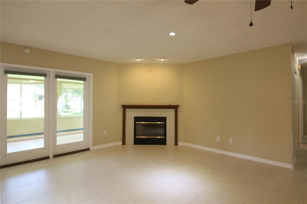 A living room features beige tile flooring, a corner fireplace, and glass doors to a patio — 1311 GLENVIEW LANE, LAKELAND, FL