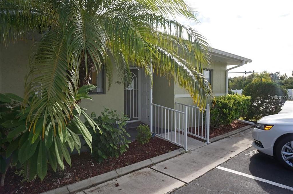 A palm tree shades the entrance of a single-story building with a white metal railing — 25225 RAMPART BOULEVARD UNIT 1404, PUNTA GORDA, FL