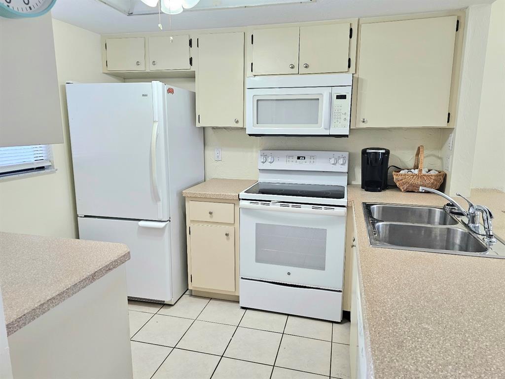 A kitchen features white appliances, light-colored cabinets, a double sink, and beige tile flooring — 25225 RAMPART BOULEVARD UNIT 1404, PUNTA GORDA, FL