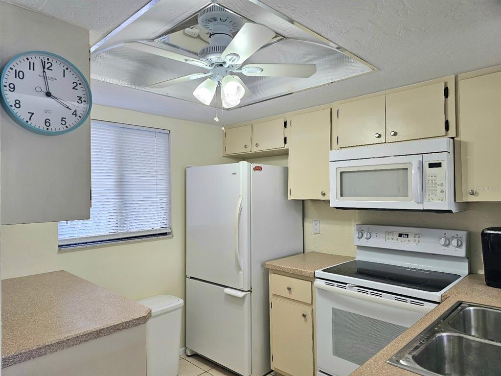 A kitchen features white appliances, light-colored cabinets, a ceiling fan, and a wall clock — 25225 RAMPART BOULEVARD UNIT 1404, PUNTA GORDA, FL