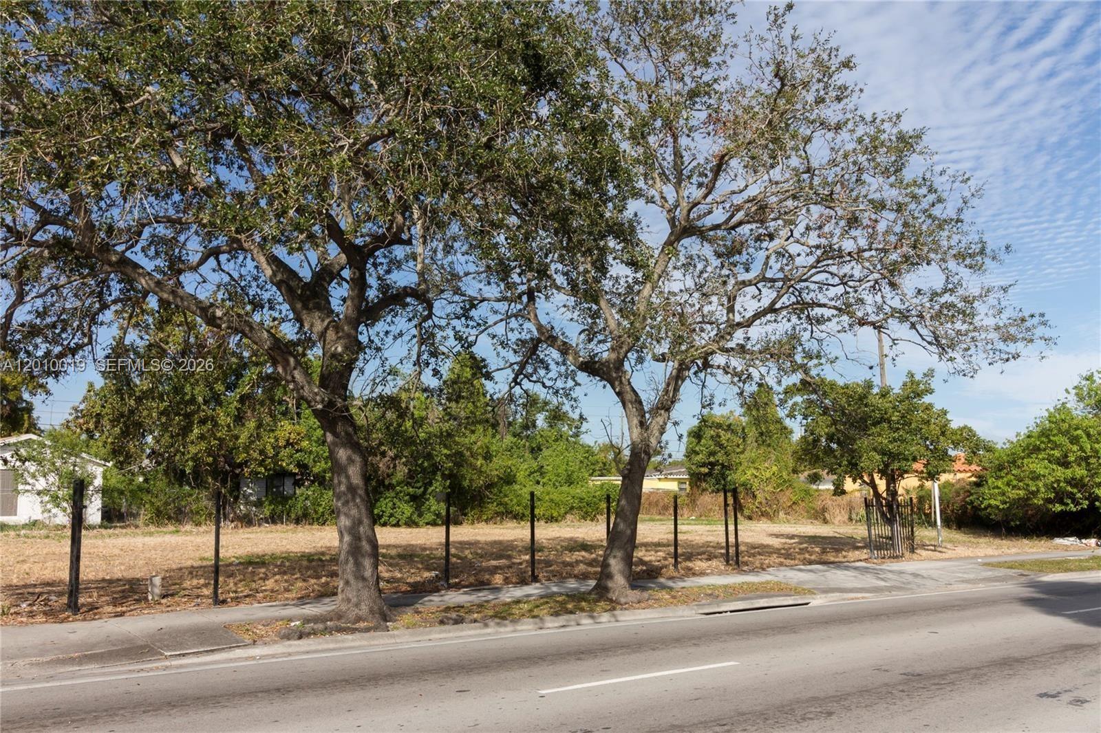A vacant, fenced-in lot features two large trees along a paved street — 1765 NW 62nd St, Miami FL 33147, MIAMI, FL