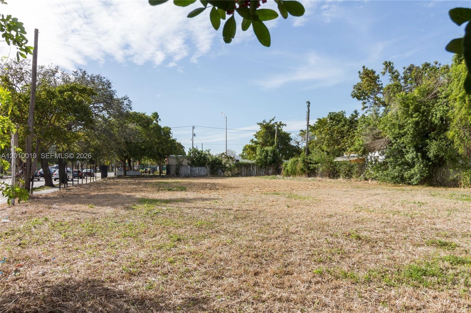 A vacant, grassy lot is enclosed by a fence with trees and a street visible — 1765 NW 62nd St, Miami FL 33147, MIAMI, FL