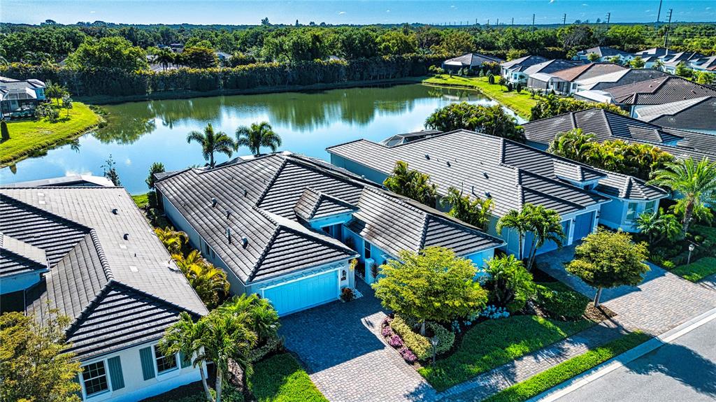 An aerial view shows several suburban houses with dark tiled roofs near a lake — 7732 SANDHILL LAKE DRIVE, SARASOTA, FL