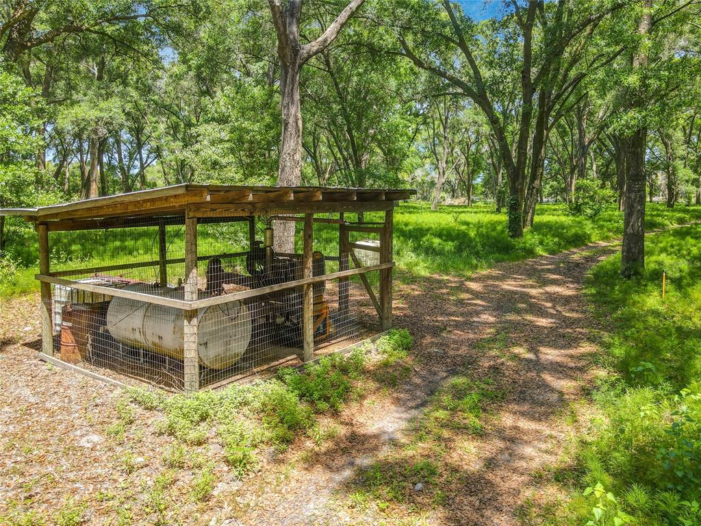 A wooden shed with a wire fence encloses a large metal tank in a wooded area — 164 DENVER ROAD, CRESCENT CITY, FL