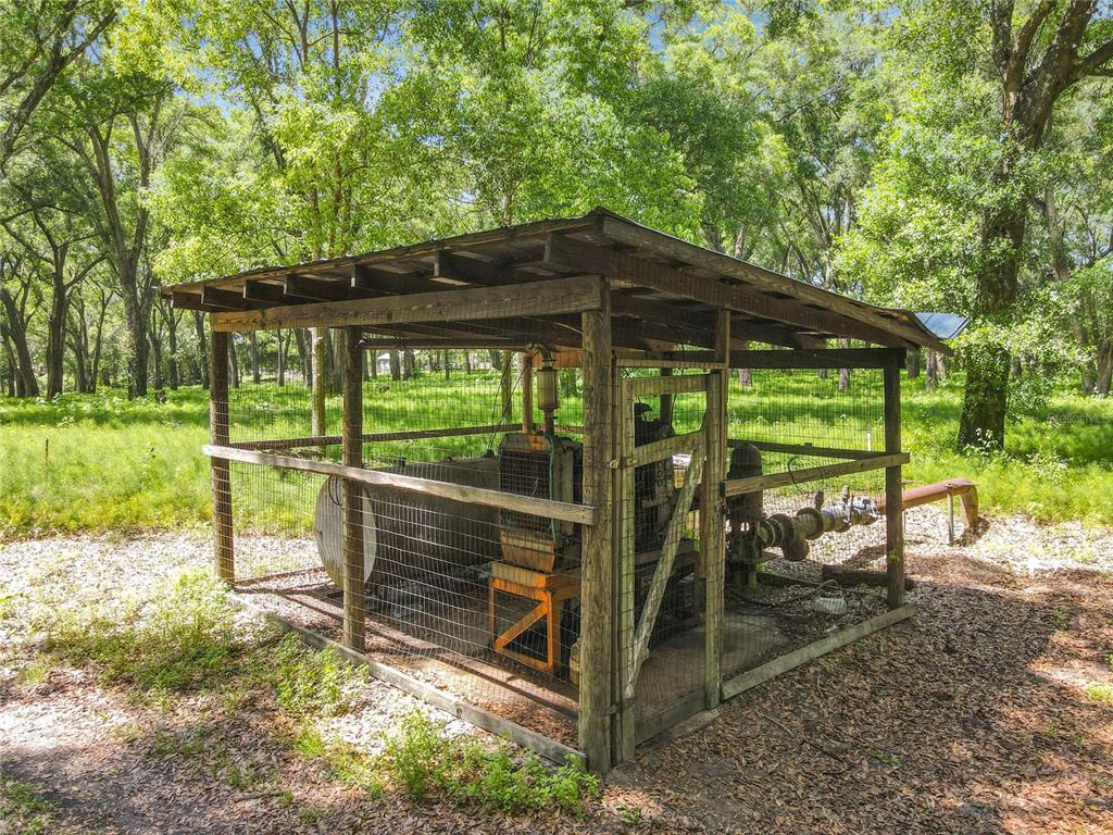A wooden shed with wire mesh walls houses a large industrial pump in a wooded area — 164 DENVER ROAD, CRESCENT CITY, FL