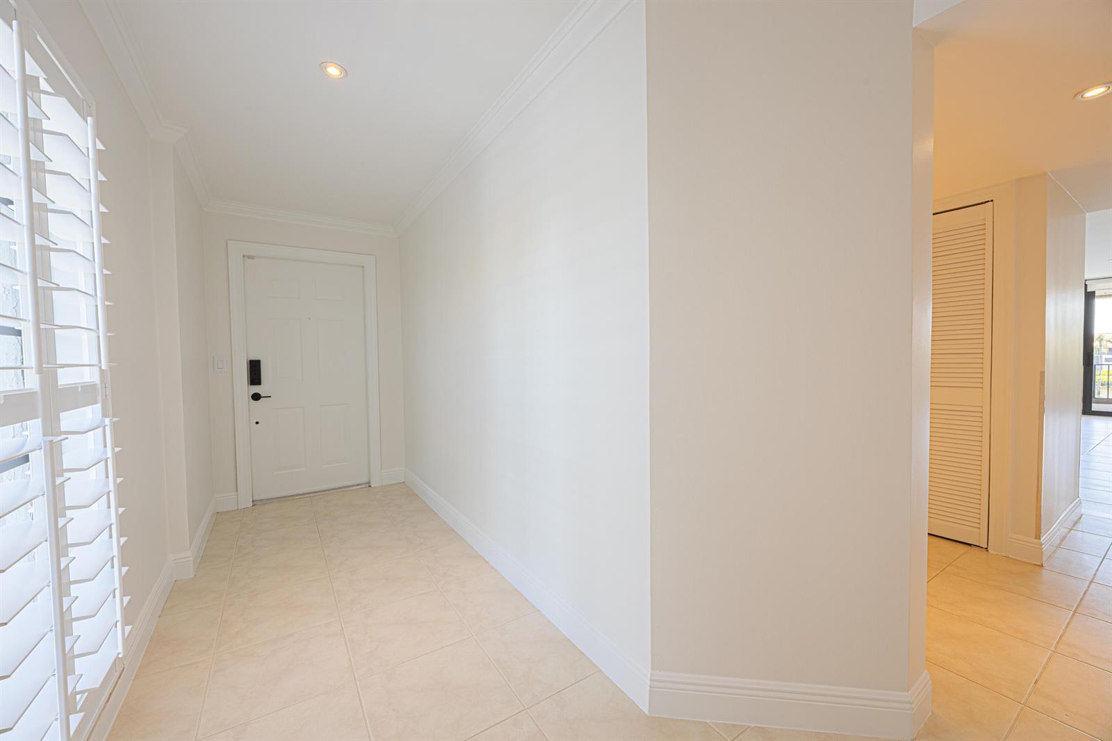 A bright entryway features white walls, tile flooring, a front door, and louvered closet doors — 801 Palm Trail # 9, Delray Beach FL 33483, DELRAY BEACH, FL