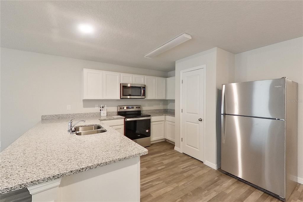 A kitchen features white cabinets, granite countertops, stainless steel appliances, and wood-look flooring — 8755 N NOBLETON WAY, DUNNELLON, FL