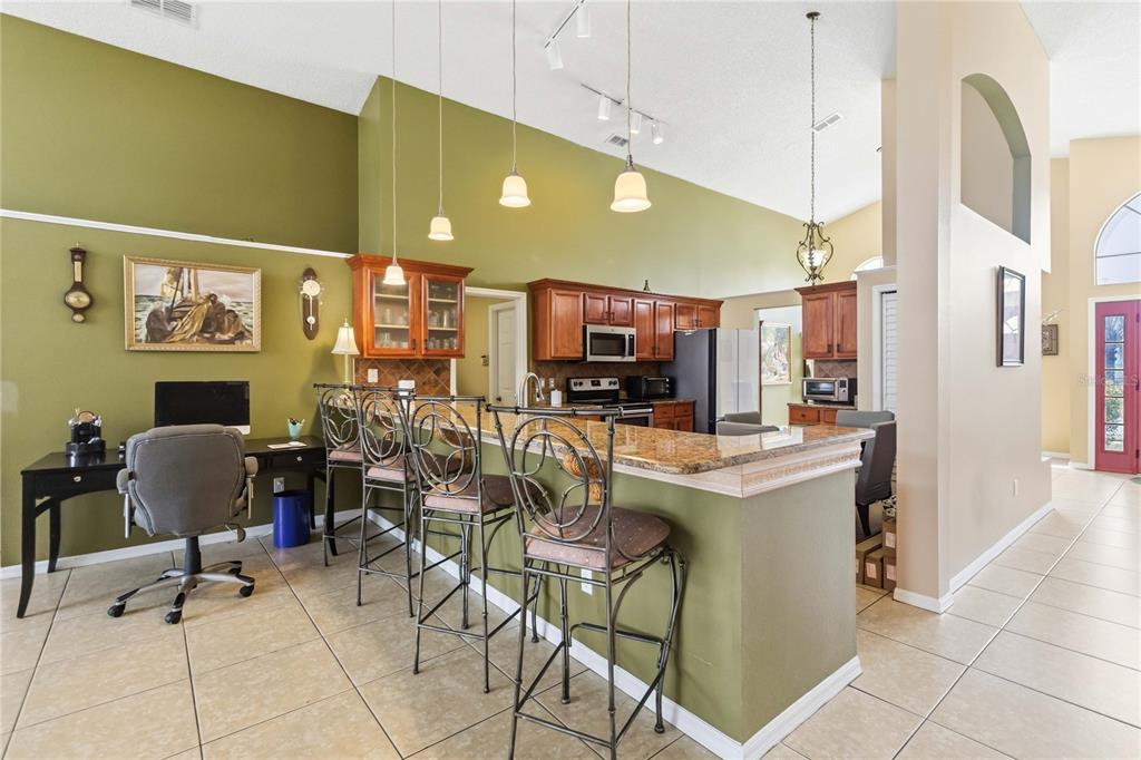 A kitchen with wood cabinets, granite countertops, and a breakfast bar overlooks a home office — 265 KASSIK CIRCLE, ORLANDO, FL