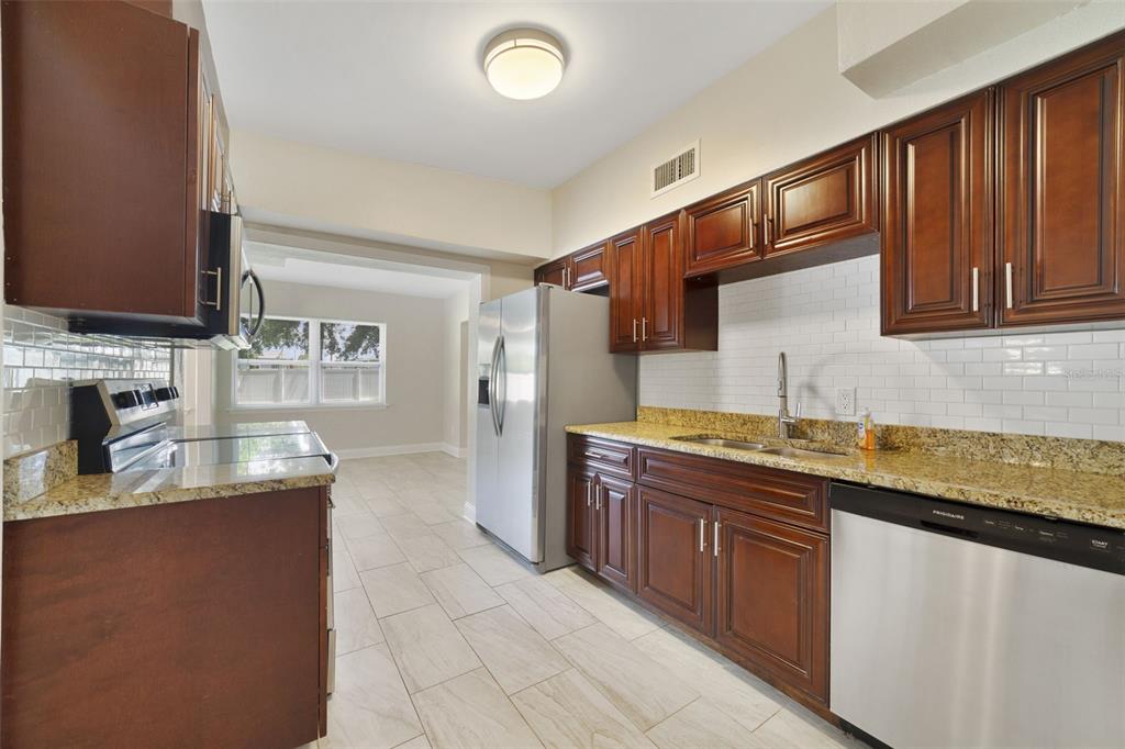 A kitchen with dark wood cabinets, granite countertops, stainless steel appliances, and light tile flooring — 1117 NEUSE AVENUE, ORLANDO, FL