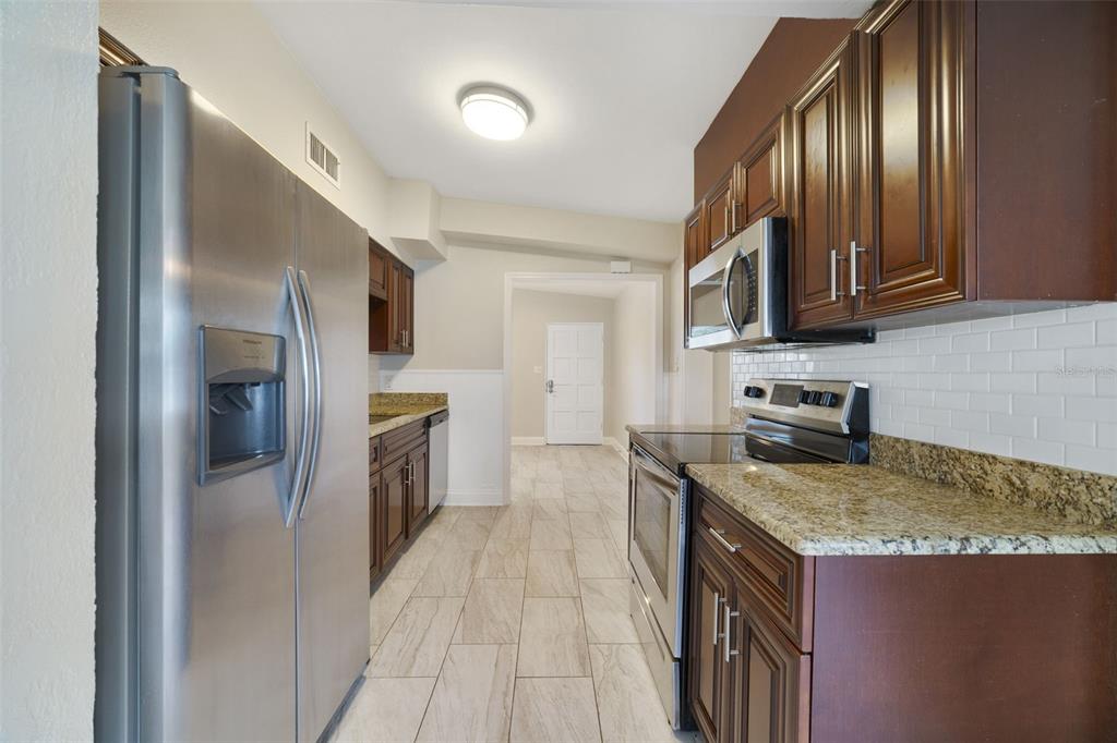 A kitchen with dark wood cabinets, granite countertops, stainless steel appliances, and light tile flooring — 1117 NEUSE AVENUE, ORLANDO, FL