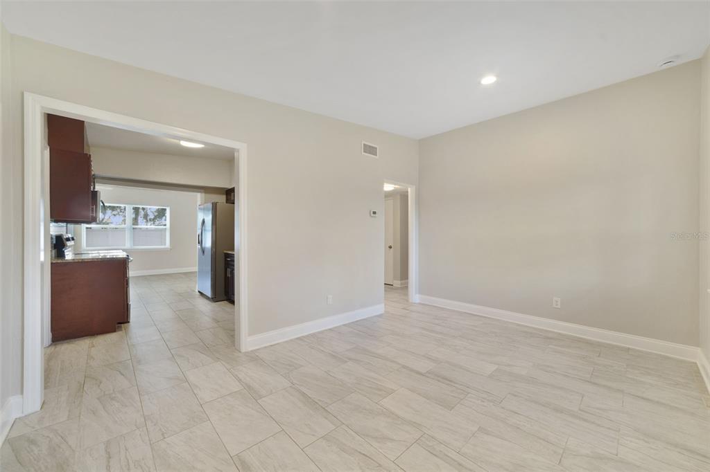 A room with light-colored tile flooring and beige walls, featuring an open doorway to a kitchen — 1117 NEUSE AVENUE, ORLANDO, FL