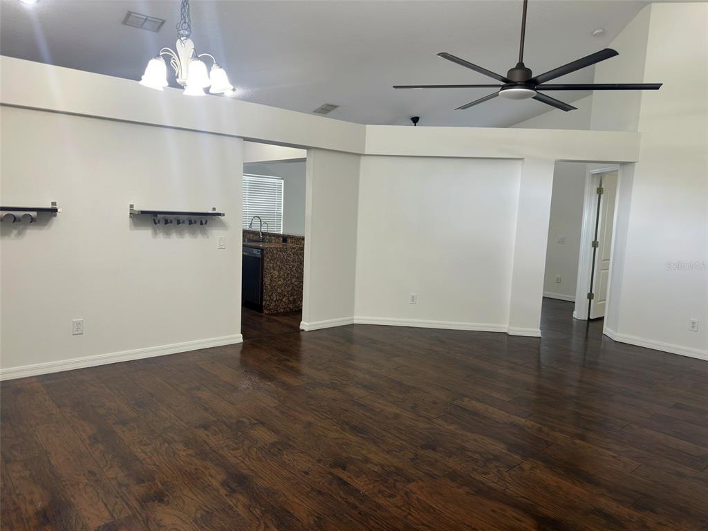 A living room with dark wood flooring, white walls, a ceiling fan, and a kitchen view — 19310 WEEDON COURT, LAND O LAKES, FL