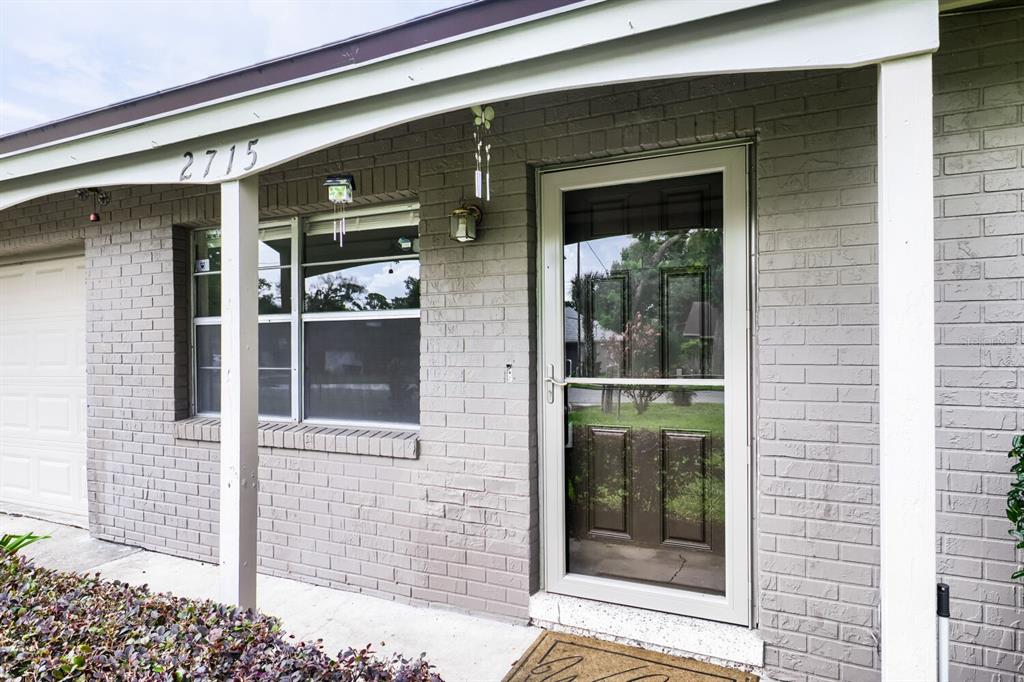 A gray brick house exterior features a front door with a storm door and windows — 2715 RAMSEY DR, APOPKA, FL