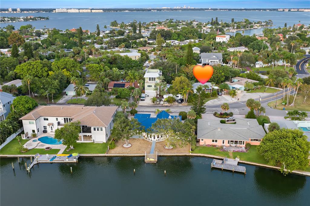 An aerial view shows waterfront houses with docks, pools, and lush landscaping along a bay — 3929 BELLE VISTA DRIVE, ST PETE BEACH, FL