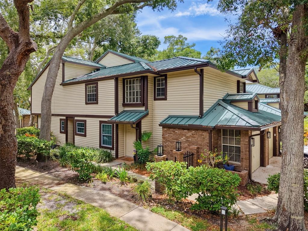 A two-story house with beige siding, a green metal roof, and brick accents — 1491 MAHOGANY LANE UNIT 1491, PALM HARBOR, FL