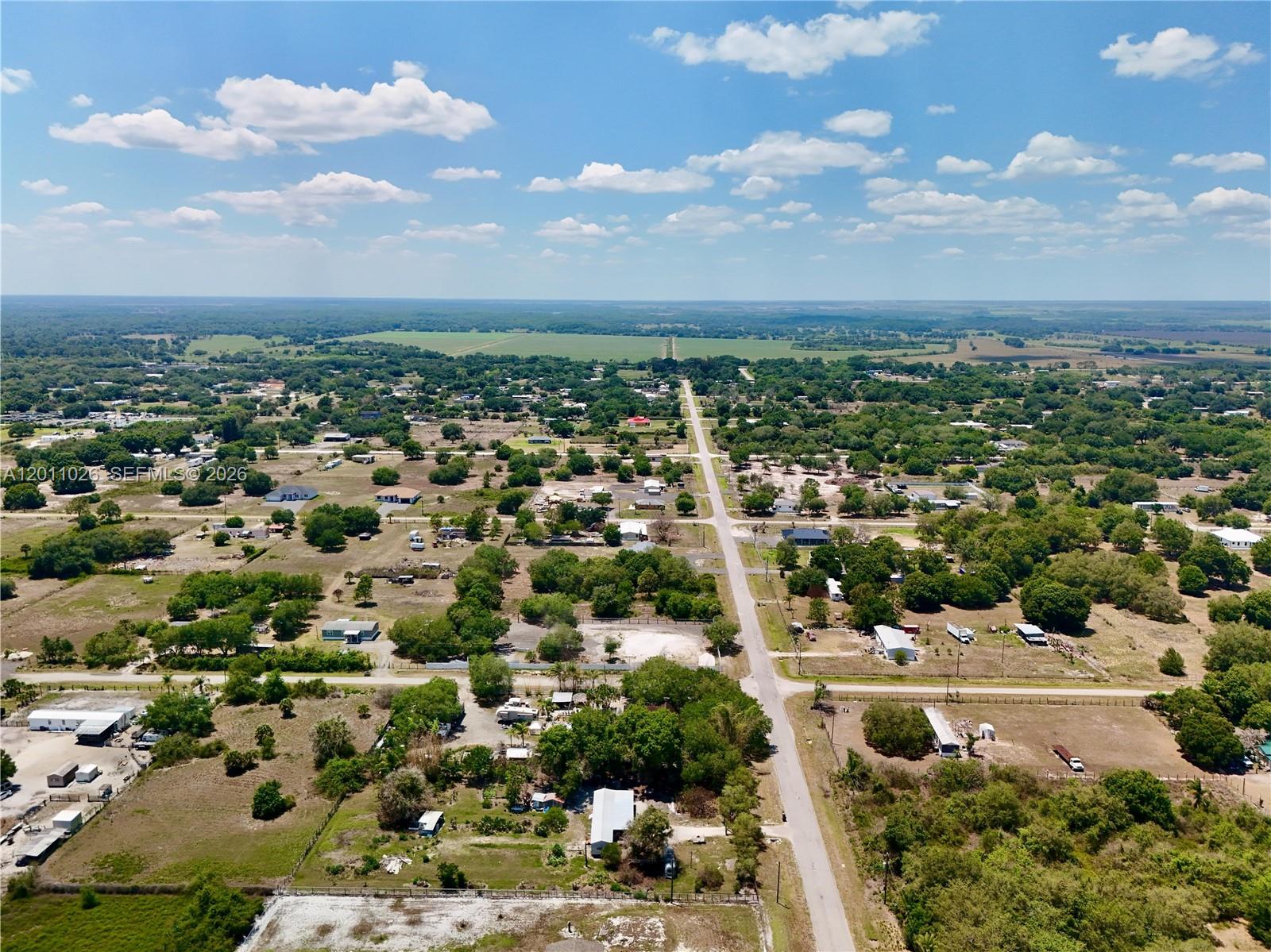 An aerial view shows a rural landscape with scattered houses, trees, and a long road — 242 BALD CYPRESS AVE, Clewiston FL 33440, CLEWISTON, FL