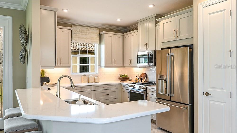 A kitchen features light-colored cabinets, stainless steel appliances, and a white quartz breakfast bar — 14525 DERNA TERRACE, BRADENTON, FL