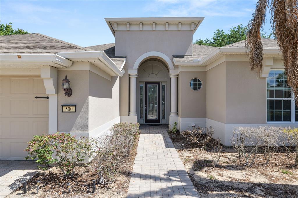 A beige house exterior features a paved walkway leading to an arched entryway with columns — 500 ARENA DRIVE, DAVENPORT, FL