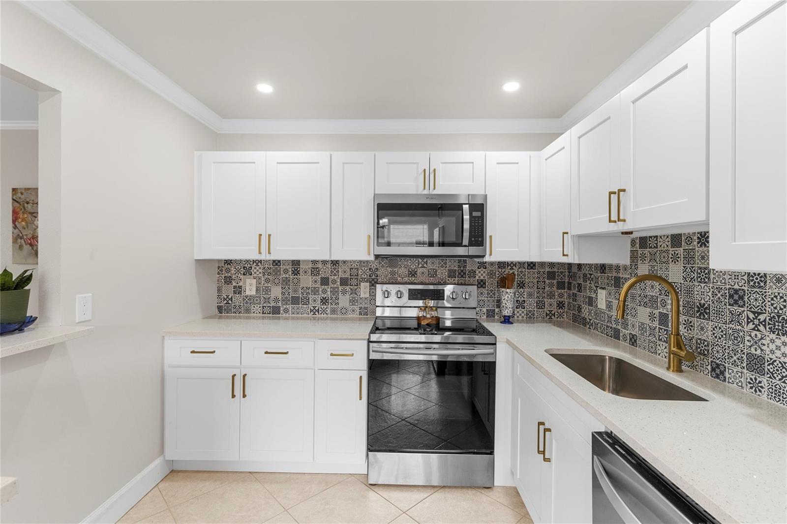 A kitchen with white cabinets, a patterned tile backsplash, stainless steel appliances, and gold hardware — 251 Seville K # 251, Delray Beach FL 33446, DELRAY BEACH, FL