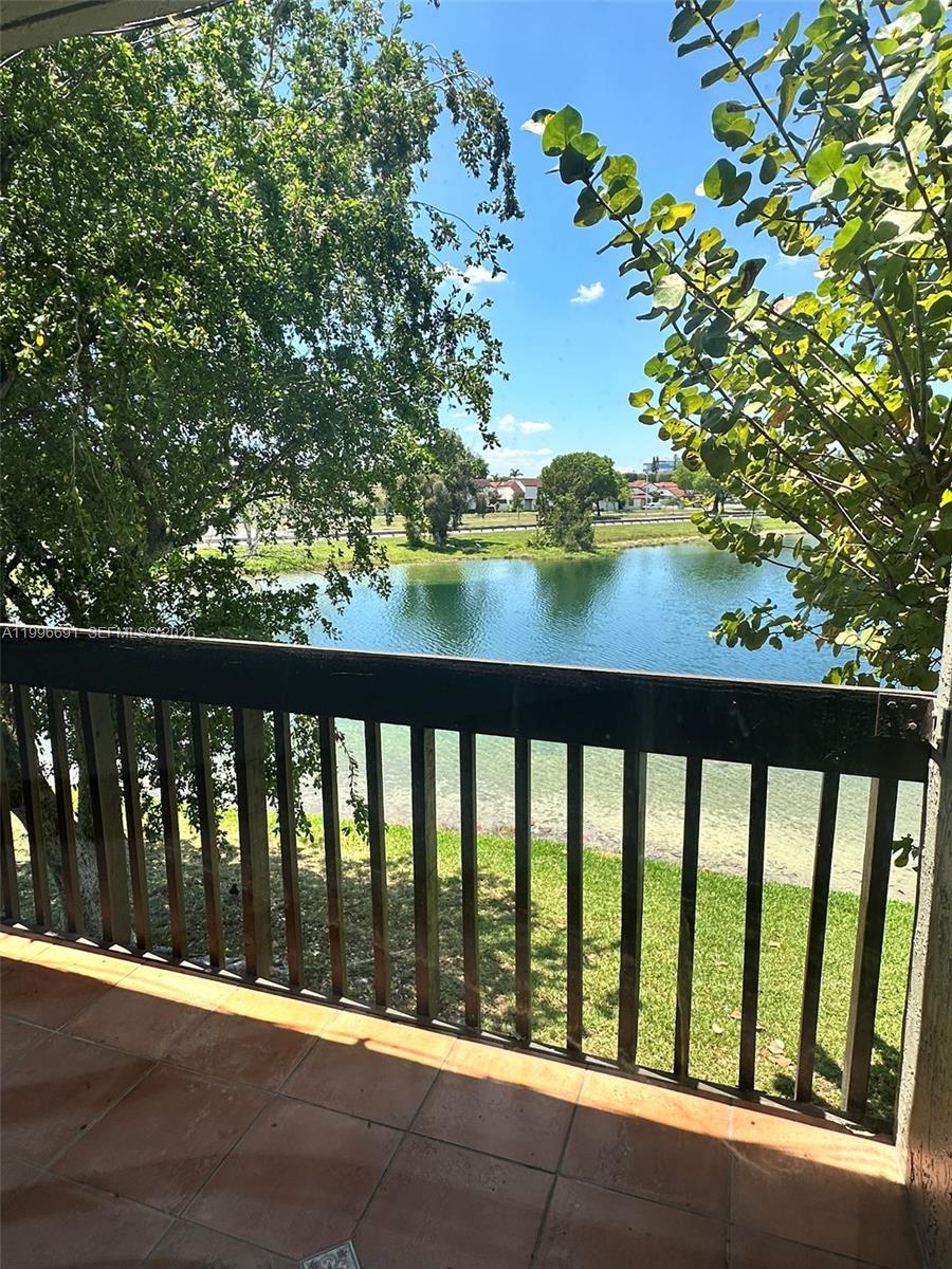 A balcony with tile flooring overlooks a lake, green lawn, and trees — 10000 NW 9th St Cir # 21, Miami FL 33172, MIAMI, FL