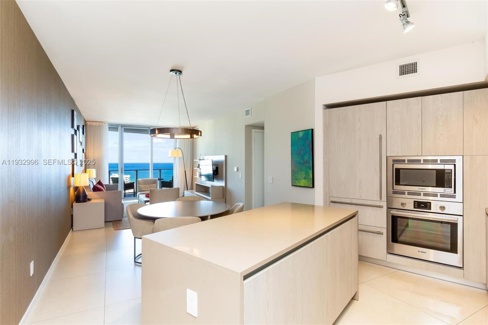 A modern kitchen with a central island overlooks a dining area and ocean view balcony — 4111 S Ocean Dr # 1910, Hollywood FL 33019, HOLLYWOOD, FL