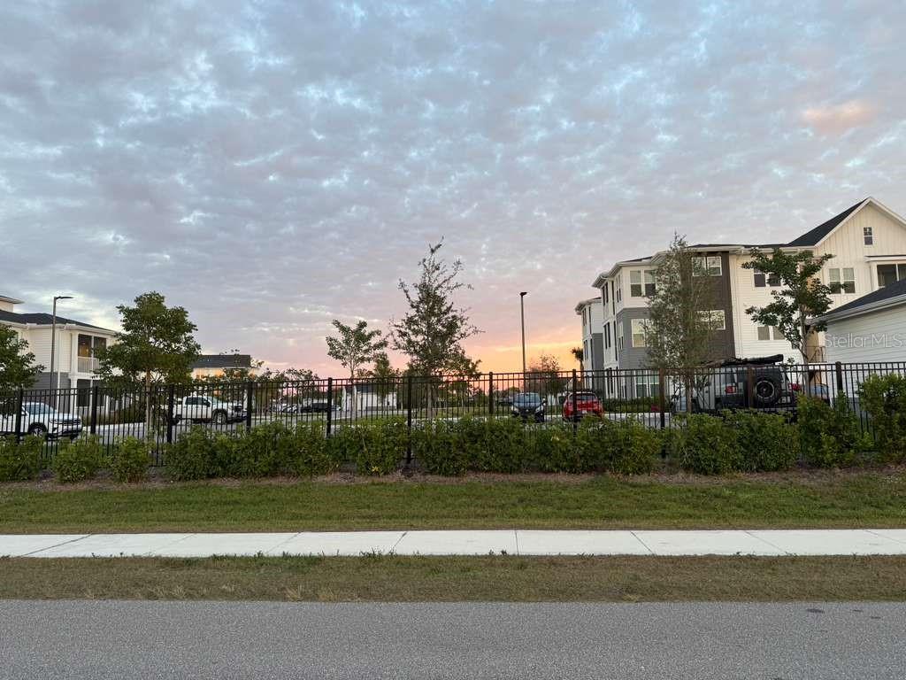 A black metal fence separates a grassy foreground from apartment buildings at sunset — 410 SW 15TH PLACE, CAPE CORAL, FL