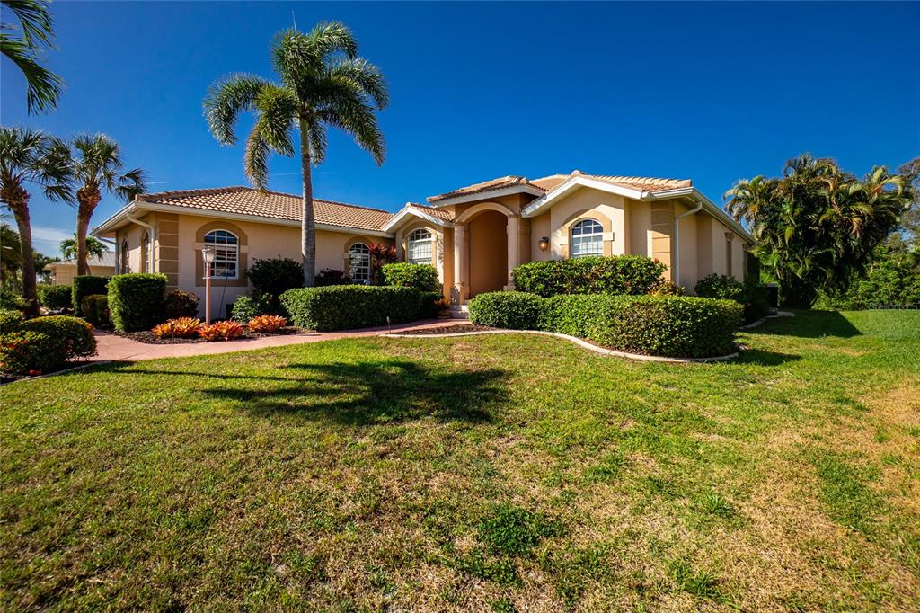 A single-story tan stucco house features a tile roof, arched windows, and manicured landscaping — 1112 MUSCOVIE COURT, PUNTA GORDA, FL