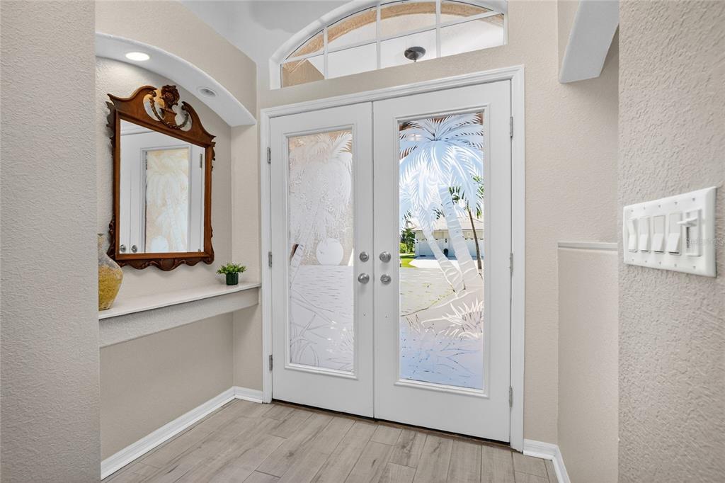 An entryway with light wood-look flooring, a wall-mounted shelf, a mirror, and etched glass doors — 1112 MUSCOVIE COURT, PUNTA GORDA, FL