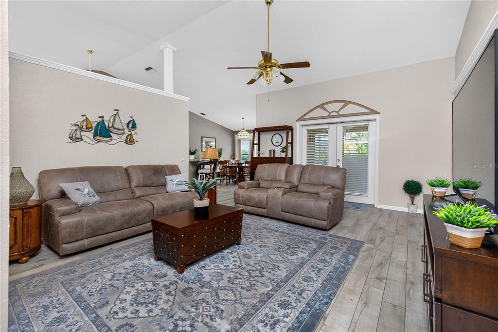 A living room features a brown sofa and loveseat, a patterned rug, and wood-look flooring — 1112 MUSCOVIE COURT, PUNTA GORDA, FL