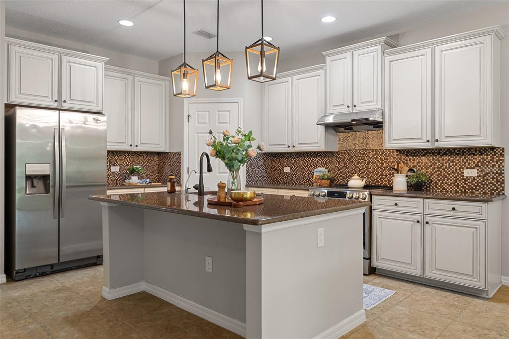 A kitchen features white cabinets, granite countertops, a center island, and a mosaic tile backsplash — 14048 WATERFORD CREEK BOULEVARD, ORLANDO, FL
