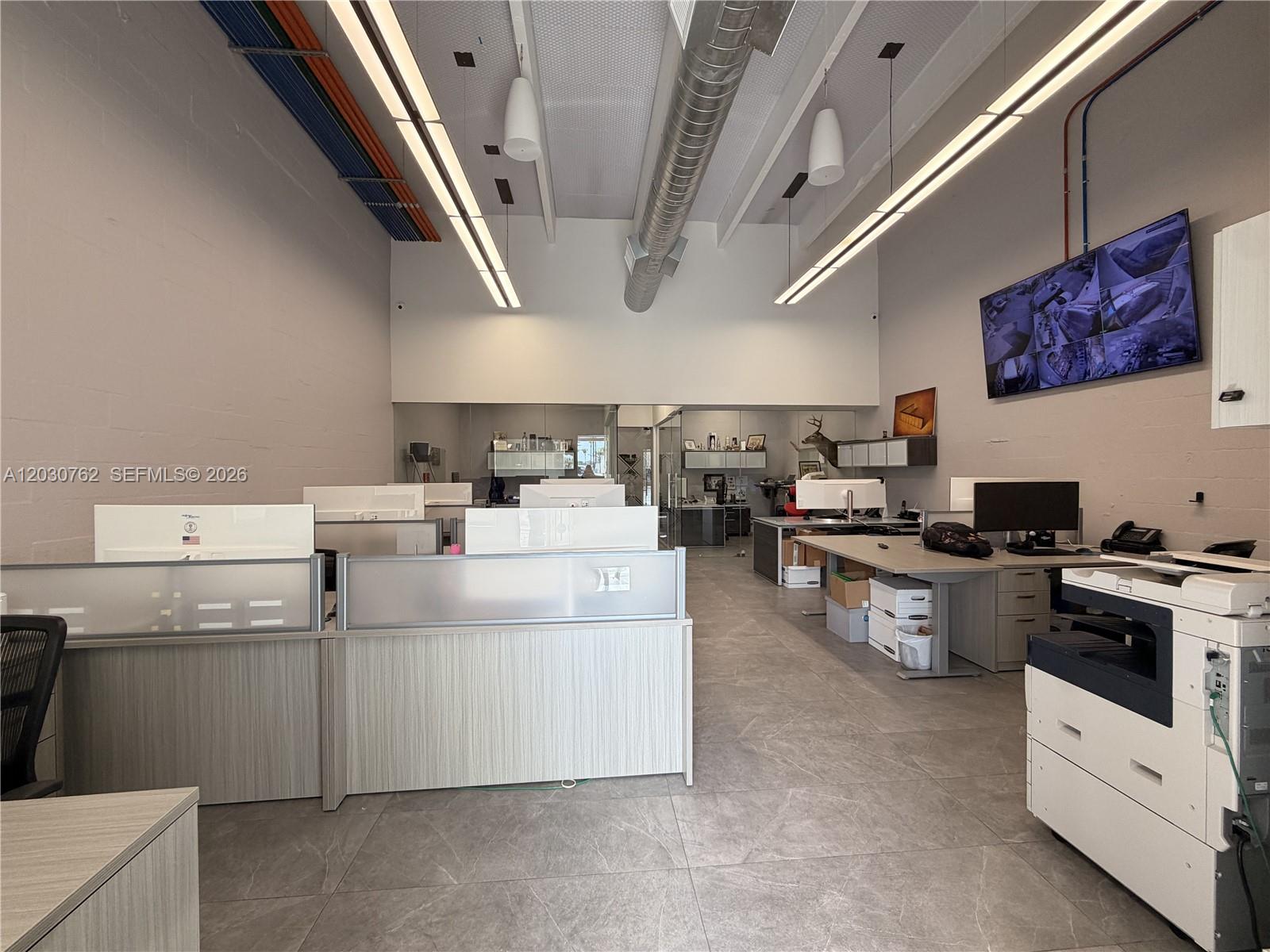 An office space features cubicles, a large printer, exposed ductwork, and a wall-mounted security monitor — 4709 SW 74th Ave, Miami FL 33155, MIAMI, FL