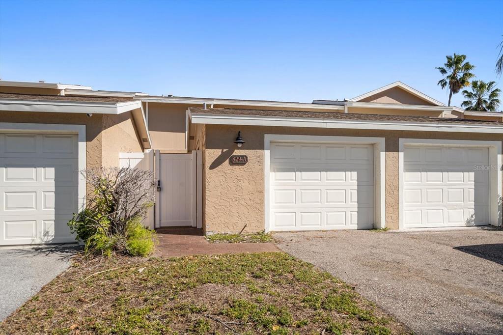 The exterior of a tan residential building features two white garage doors and a gated entrance — 829 E GULF BOULEVARD UNIT 107, INDIAN ROCKS BEACH, FL