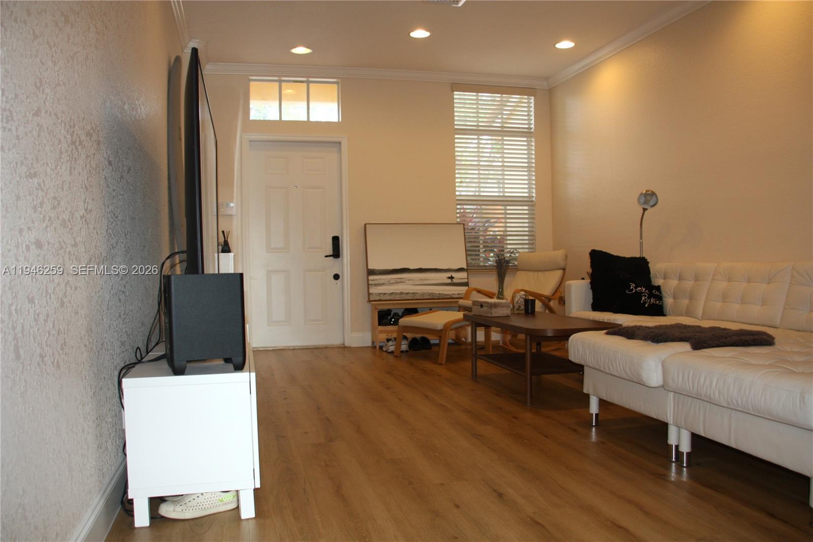A living room features light wood flooring, a white sofa, and a television on a stand — 7414 E Briella Dr, Boynton Beach FL 33437, BOYNTON BEACH, FL