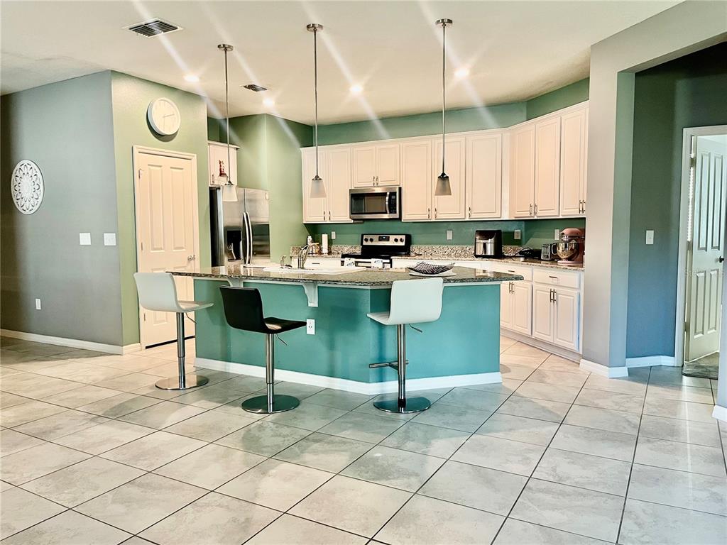 A kitchen features white cabinets, a teal island with three stools, and light tile flooring — 2860 BOATING BOULEVARD, KISSIMMEE, FL