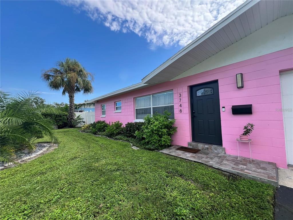 A pink exterior house features a dark front door, tiled entryway, and a palm tree — 3748 MANATEE DRIVE SE, ST PETERSBURG, FL