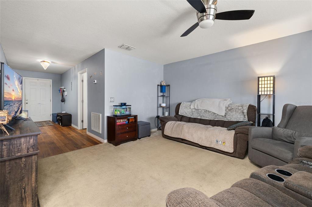 A living room features beige carpeting, a brown sofa, a recliner, and a ceiling fan — 1321 WOODLARK DRIVE, HAINES CITY, FL