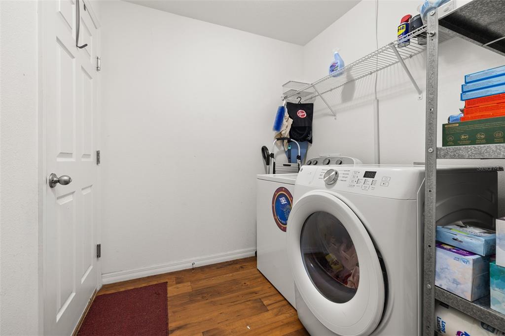 A laundry room features a white front-loading washer, wood-look flooring, and wire shelving — 1321 WOODLARK DRIVE, HAINES CITY, FL