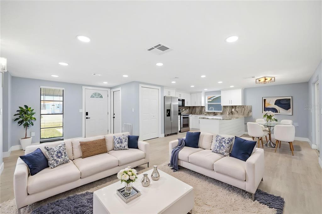 An open-concept living room and kitchen featuring white cabinetry, light wood floors, and two sofas — 12824 1ST ISLE, HUDSON, FL