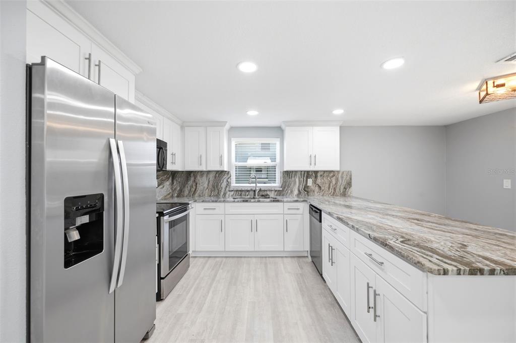 A kitchen features white cabinets, stainless steel appliances, and a dramatic brown-and-white stone backsplash — 12824 1ST ISLE, HUDSON, FL