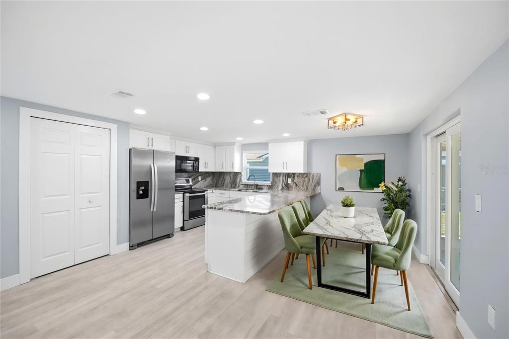 A kitchen and dining area with white cabinets, marble countertops, and light wood flooring — 12824 1ST ISLE, HUDSON, FL