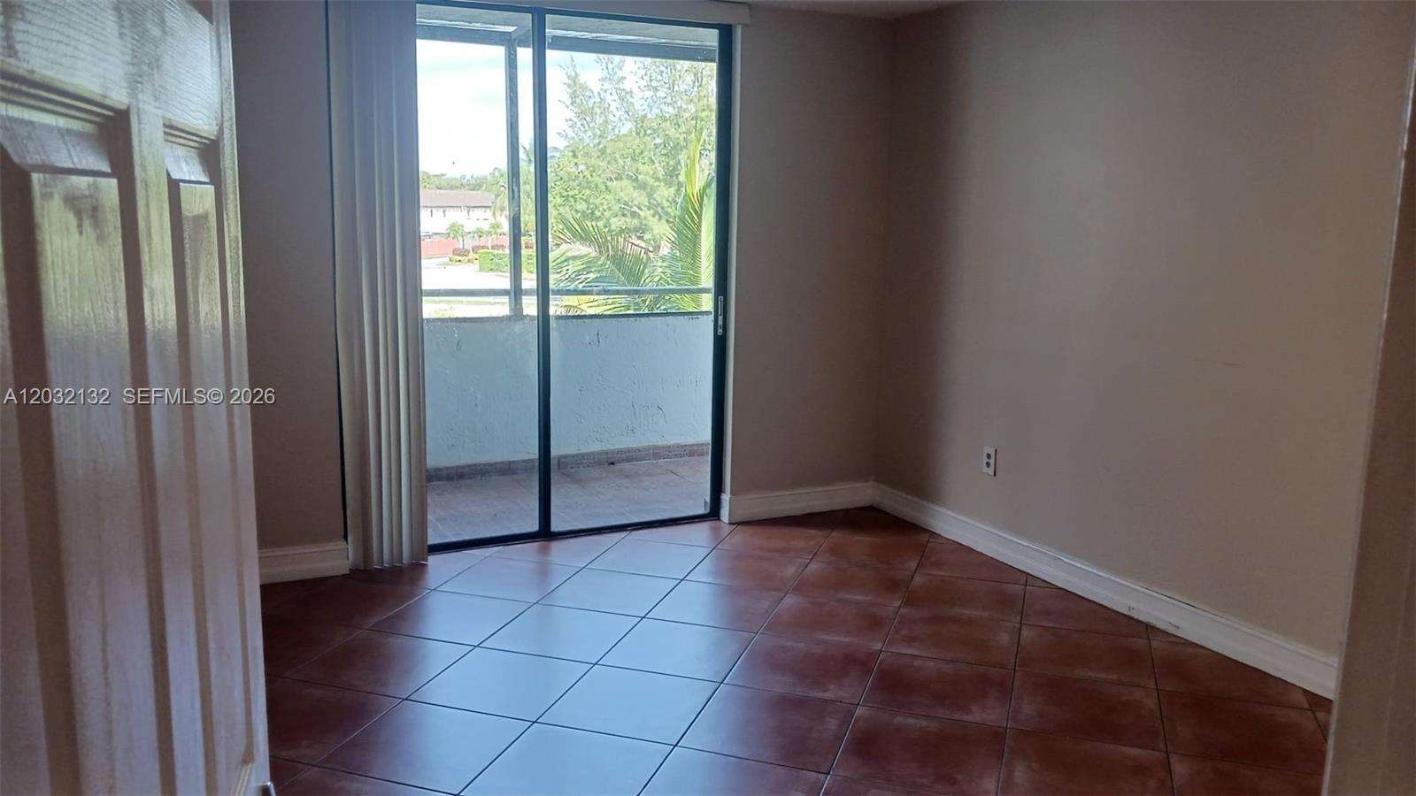 An empty room features brown tile flooring, beige walls, and a sliding glass door to a balcony — 8335 SW 152nd Ave # 310, Miami FL 33193, MIAMI, FL