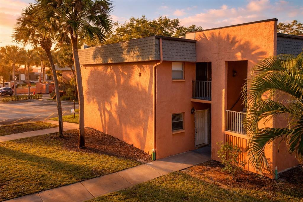 An exterior view of a two-story peach-colored apartment building with palm trees at sunset — 4805 ALT 19 UNIT 311, PALM HARBOR, FL