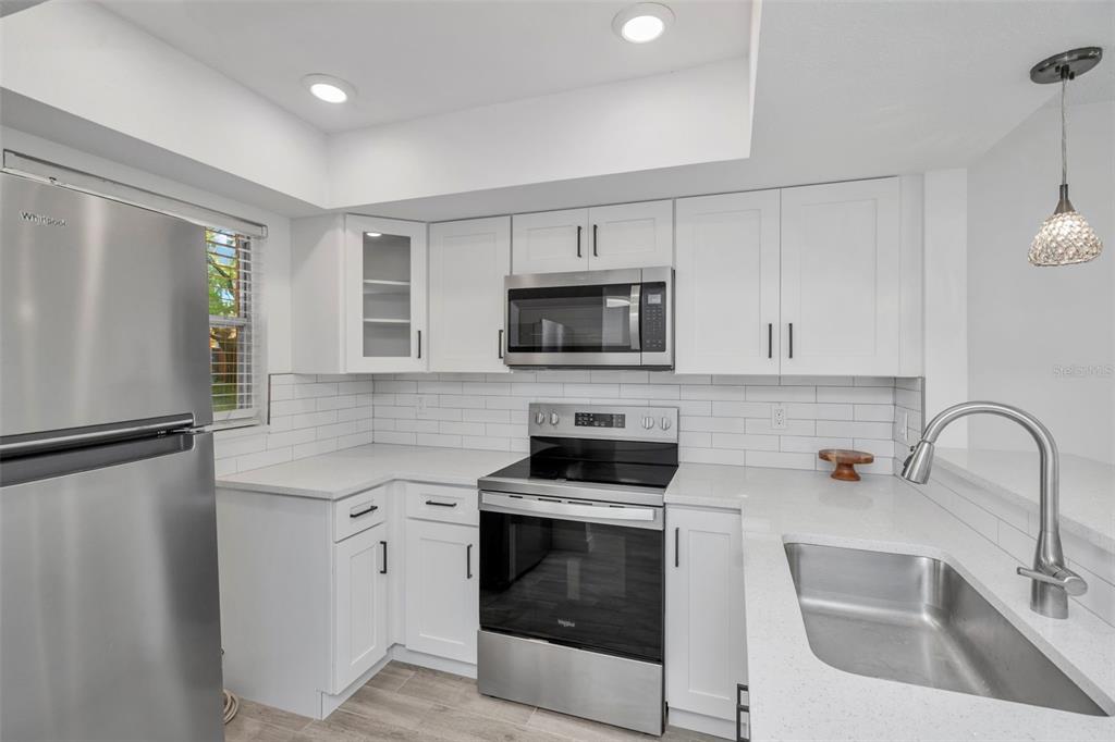 A kitchen features white cabinets, stainless steel appliances, quartz countertops, and a subway tile backsplash — 4805 ALT 19 UNIT 311, PALM HARBOR, FL