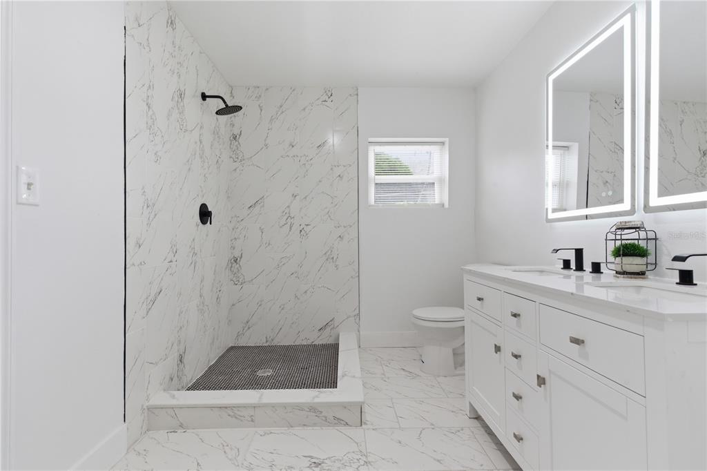 A modern bathroom features a marble-tiled walk-in shower, a double vanity, and a toilet — 923 1ST AVENUE NW, LARGO, FL